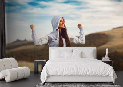 Young sport woman with raised arms motivates herself in nature Wall mural