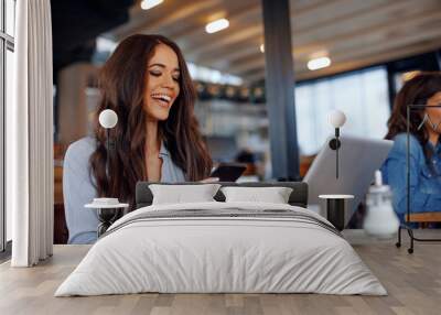 young woman texting on the phone with a laptop on table in cafe Wall mural