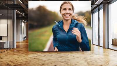 Beautiful adult woman is jogging outdoor on cloudy day in autumn. Wall mural