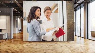 Businesswoman owning small business store. She is talking with a customer who is choosing the goods. Wall mural