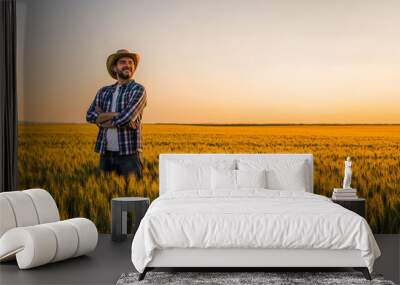 Farmer is standing in his growing wheat field. He is happy because of successful sowing. Wall mural