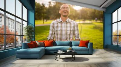 Portrait of cheerful adult man in park who is using smartphone. Wall mural