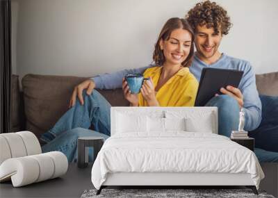 Portrait of young happy couple at home. They are relaxing at sofa. Wall mural