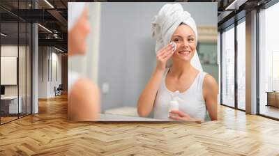 Portrait of young woman who is cleaning skin on her face. Wall mural