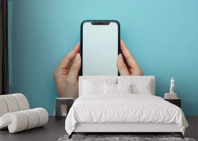 A person holding a black phone with a blank screen in front of a blue background. Wall mural