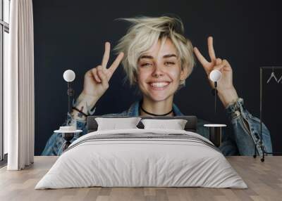 A blonde woman with a short haircut in the studio shows a victory sign and smiles widely Wall mural