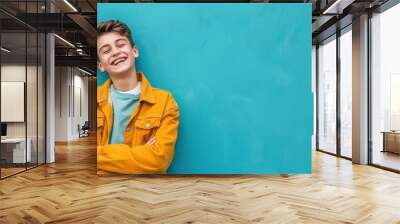 A cheerful teenage boy laughing and looking at the camera dressed in trendy casual clothes vibrant blue background with copy space Wall mural