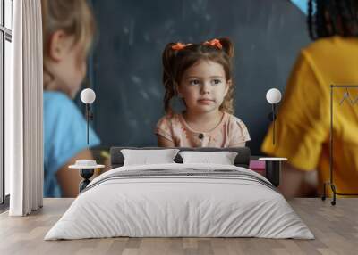 A cute little girl practicing pronunciation with a speech therapist colorful phonetic cards scattered on the table in front of them Wall mural