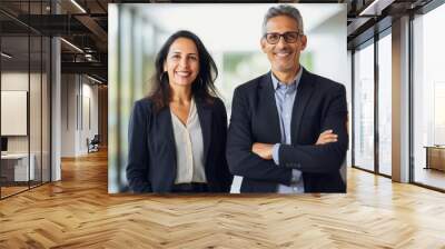 Portrait of smiling mature Latin or Indian business man and European business woman standing arms crossed in office. Two diverse colleagues. Group team of confident professional business people. Wall mural