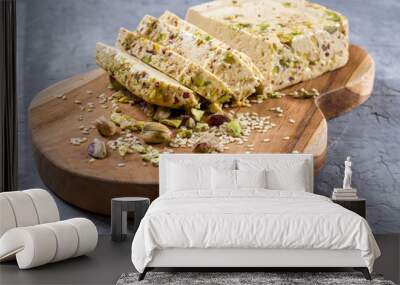 Sesame halva with pistachios on a teak chopping board on a grey background. Wall mural