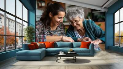 Smiling female caregiver assisting senior woman doing puzzle at home Wall mural