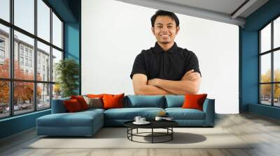 young asian man smiling happy at the camera with arms crossed wearing black polo t shirt isolated on white background Wall mural