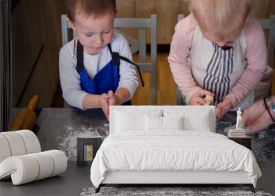 Two young children wearing aprons are making cookies in a kitchen, using cookie cutters and dough on a flour-covered countertop Wall mural