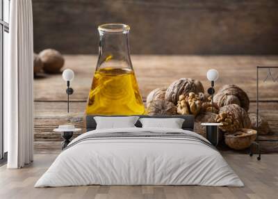 Glass bottle with walnut oil and walnut kernel on a wooden table. Cosmetic and therapeutic product. Wall mural