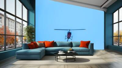 A small two seater commercial helicopter set against a clear, blue sky passes from bottom to top Wall mural