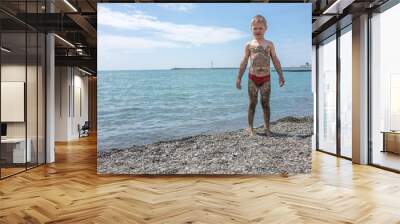 The boy is covered with small pebbles after lying on the beach Wall mural