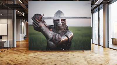 Antique knight in the plate armor and helmet holds a sword in hands close up. Wall mural