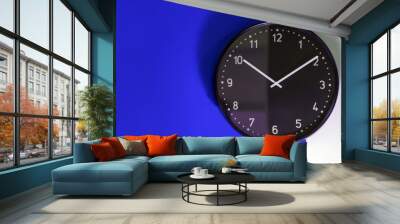 Black clock on a blue and white wall Wall mural