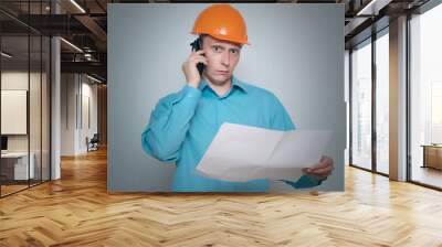 Builder construction worker with mobile phone is holding in hand a plan draft document isolated on gray background. Wall mural