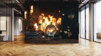 Crystal ball, magic book, magic potion and other wizard accessories on a table on a burning fire background. Wall mural