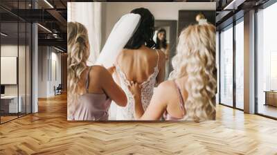 Back view of a bride in a wedding dress and bridesmaids helping her to dress Wall mural