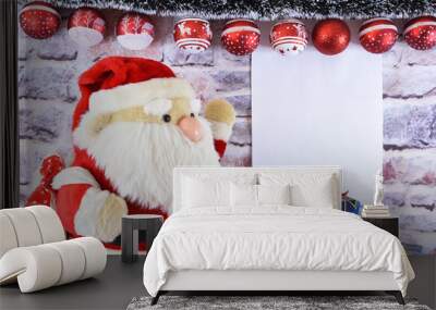 A plush Santa Claus stands next to New Year's gifts, and a blank page for congratulations hangs on the wall Wall mural