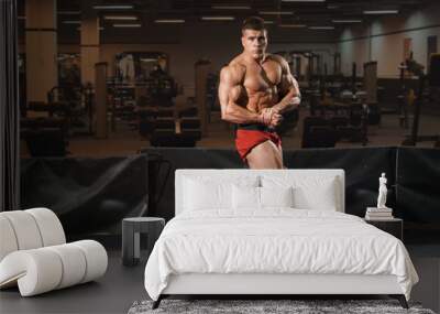 Young man bodybuilder standing in gym and posing Wall mural