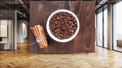 Grains of coffee in white bowl and bunch of cinnamon sticks on wooden background Wall mural