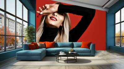 Beautiful blonde woman makeup artist hold red lipstick rouge on red Wall mural