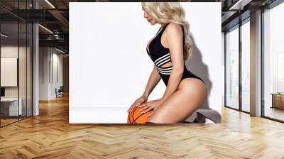 Beautiful sexy fitness blonde woman in black swimsuit, high sport socks and sneakers sitting and holding ball Wall mural