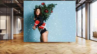 Beautiful sport athletic girl  run with Christmas tree holds red New Year presents gift box happy smiling laughing on blue  Wall mural