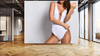 Closeup of young beautiful slim woman in white one-piece swimsuit with deep neckline posing over white background Wall mural