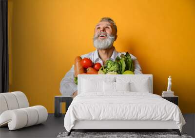 Cool old mature senior man with gray beard shopping hold grocery shopping bag with healthy organic vegetables on yellow Wall mural