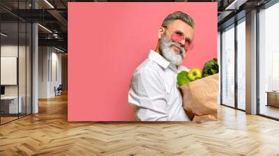 Cool old mature senior man with gray beard shopping hold grocery shopping bag with healthy organic vegetables Wall mural