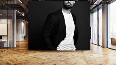 Handsome brutal man in stylish casual clothes and jacket standing with hands in pockets and looking at camera over dark background. Stylish business casual style for men Wall mural