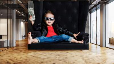 impudent kid boy millionaire in leather jacket and red t-shirt is sitting lounging in armchair holdi Wall mural