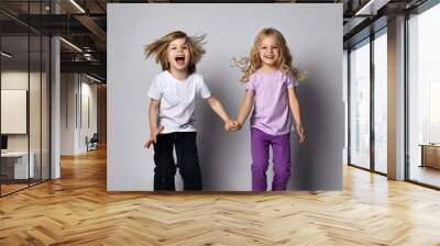 Little positive baby girl and boy in stylish casual clothing holding hands and smiling Wall mural