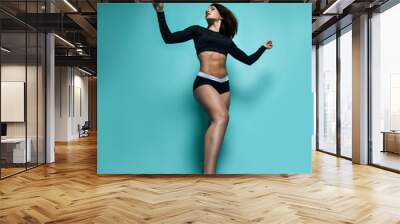 Positive athletic brunette woman in black sportswear shorts crop top with sleeves and sneakers is dancing Wall mural