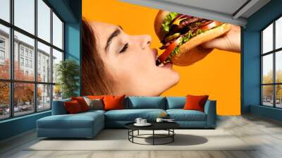 Woman eat burger sandwich with hungry mouth on yellow background Wall mural