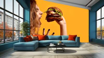 Woman hold big beef burger sandwich with hungry mouth happy screaming laughing on yellow background Wall mural