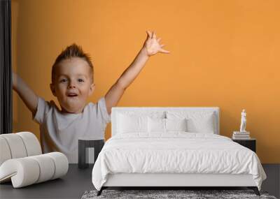 Young boy kid in white t-shirt celebrating happy smiling laughing with hands spreading up on yellow Wall mural