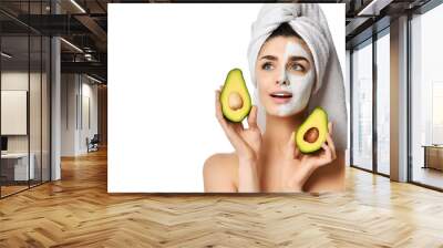 Young pretty woman whalf of face in facial mask and with the other half clean holds cut in half fresh avocado. Beauty skin care  Wall mural