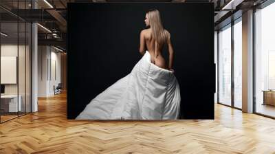 Young sensual sexy naked feminine woman stands back to camera covering herself with large soft white blanket, looking aside over black background. Fashion, vogue, sexy stylish look for woman concept Wall mural