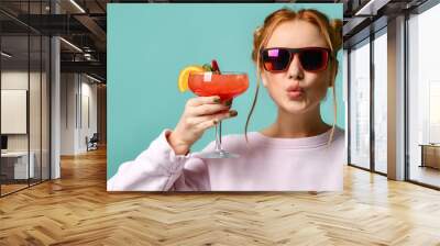 Young woman in stylish sunglasses raises her glass with tropic cocktail strawberry margarita to us and sends a kiss Wall mural