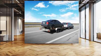 A crossover with trailer towing a car on the countryside road in motion against sky with clouds Wall mural