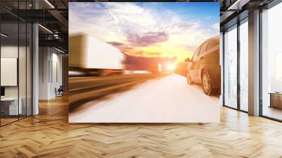 Abstract background with two trucks in motion and a car on the winter road against a sky with a sunset Wall mural