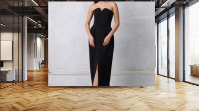 Beautiful brunette female model dressed in strapless taupe black formal dress posing in studio. Attractive smiling young woman in elegant evening outfit standing against white wall on background. Wall mural