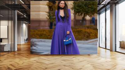 Young beautiful caucasian woman with long straight hair and makeup in purple trousers and long coat cape standing and posing at city street in autumn Wall mural