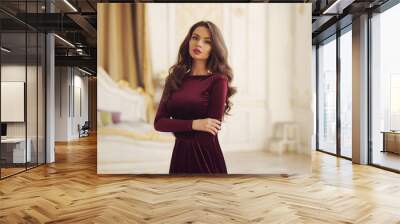 Young beautiful pretty elegant woman with long curly hair wearing cherry red evening dress and posing in bright inteiror Wall mural