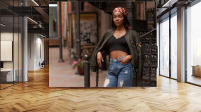 Young beautiful stylish african woman standing and posing. Girl in jeans and green jacket. Outdoor summer fashion lifestyle portrait. Wall mural